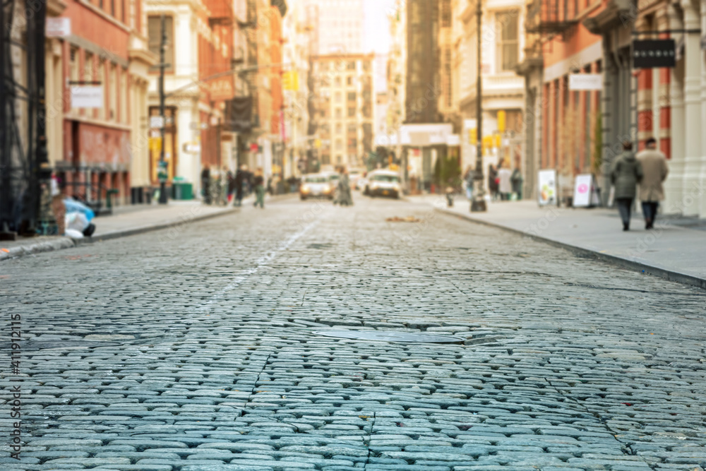Obraz premium Cobblestone street with crowded intersection blurred in the sunlit background - SoHo, New York City