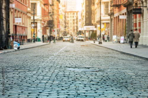 Cobblestone street with crowded intersection blurred in the sunlit background - SoHo  New York City