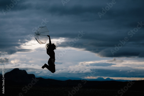 silhouette of a young woman jumping while holding an umbrella isolated on a cloud background. Jumping woman