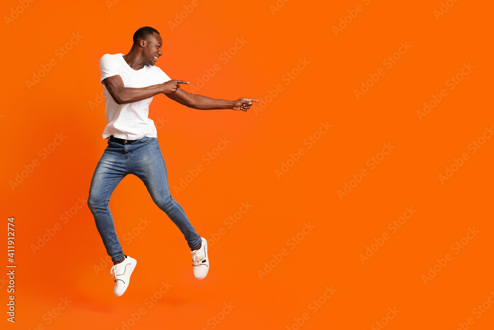 Millennial african american man pointing at copy space while jumping