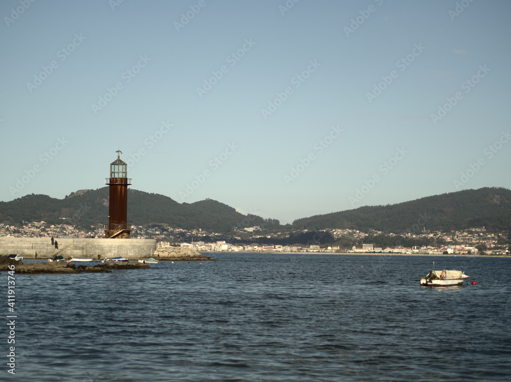 The bay and the lighthouse in the sunny day with the sea in the background.