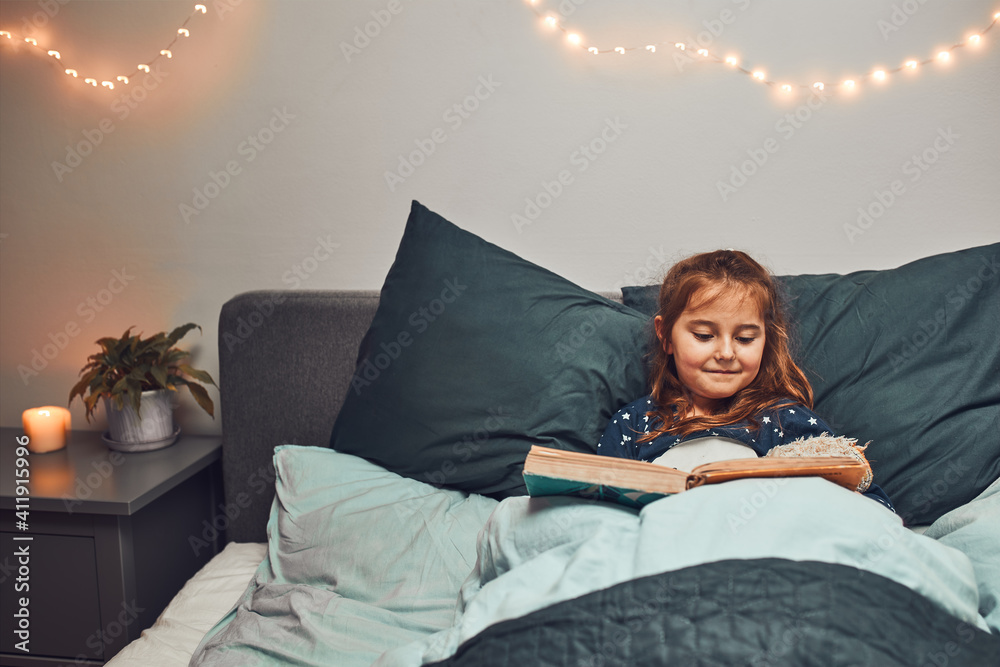 Little girl reading book and watching pictures in bed before going to
