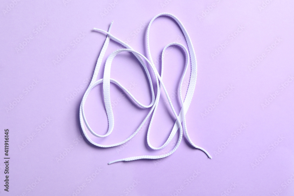 White shoelaces on lilac background, flat lay