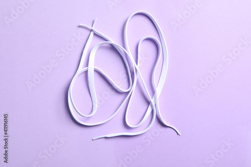 White shoelaces on lilac background, flat lay