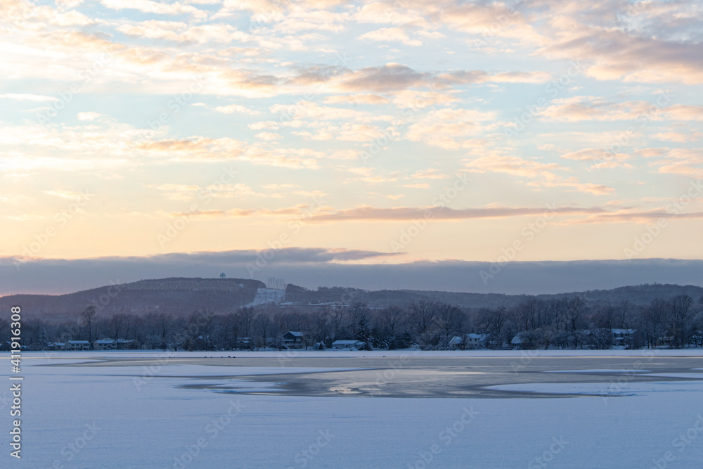 snow covered lake, light blue cloudy sky with orange sunset glow