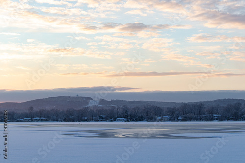 snow covered lake, light blue cloudy sky with orange sunset glow © Kevin