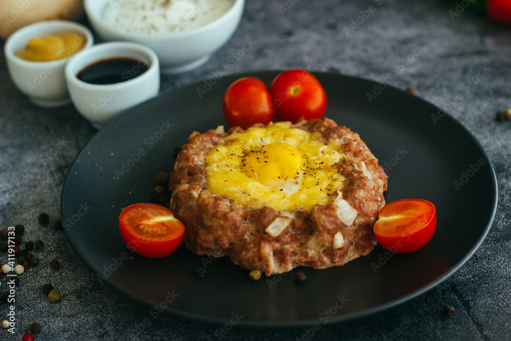Beefsteak with egg on a plate. Delicious hot dish. The dish is decorated with cherry tomatoes and herbs. Beefsteak on a plate Beefsteak with egg on a plate. Delicious hot dish. The dish is decorated with cherry tomatoes and herbs. Beefsteak on a plate