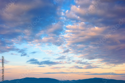 cloudscape in summer at sunrise. clouds on the blue sky in yellow and pink morning light. idyllic weather condition, picturesque scenery above the mountain ridge