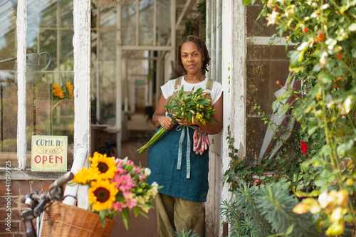 Portrait confident female florist with bouquet in shop doorway