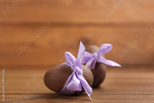 Sweet chocolate eggs with violet bows on wooden table. Space for text