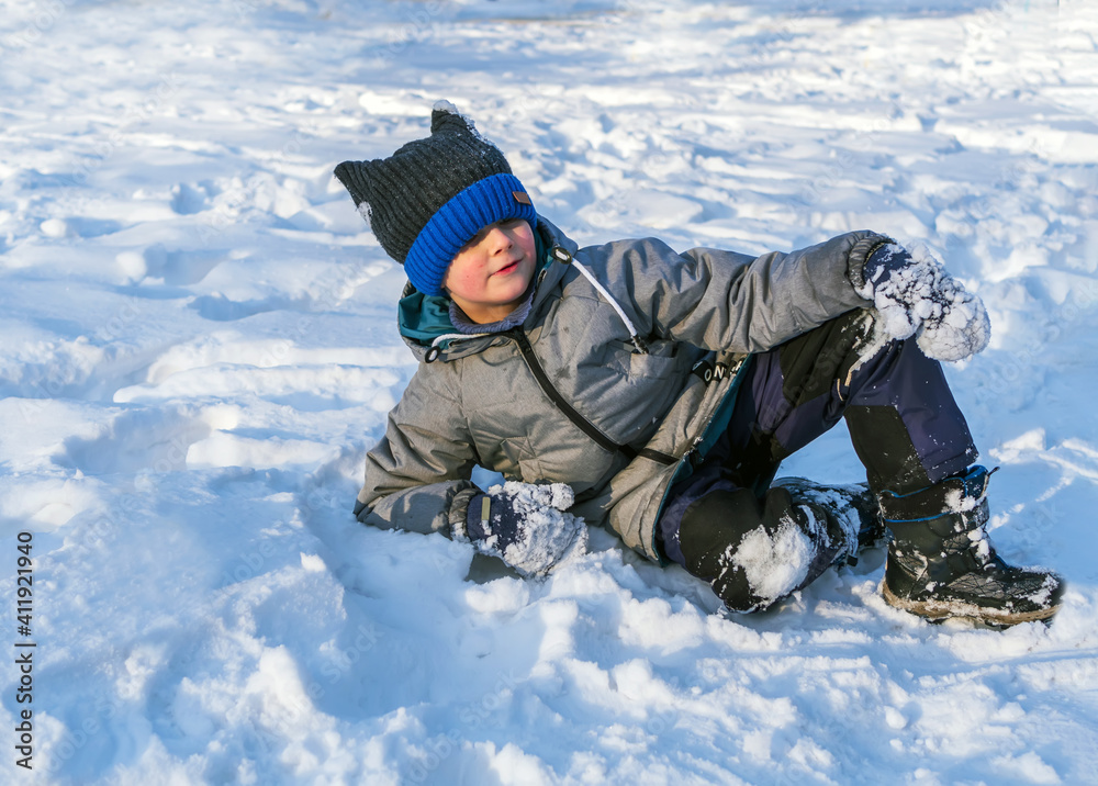 Smiling caucasian boy in green jacket and blue knit cap is lying on the snow. Smiling caucasian boy in green jacket and blue knit cap is lying on the snow.