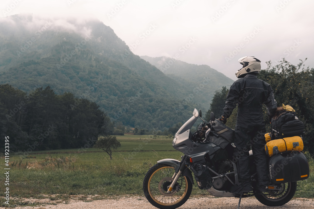 A motorcycle driver with motorbike look distance, Adventure vacation, biker dressed in raincoat. sealed bag, water resistant, overalls. Mountains road trip, side bags equipment. copy space