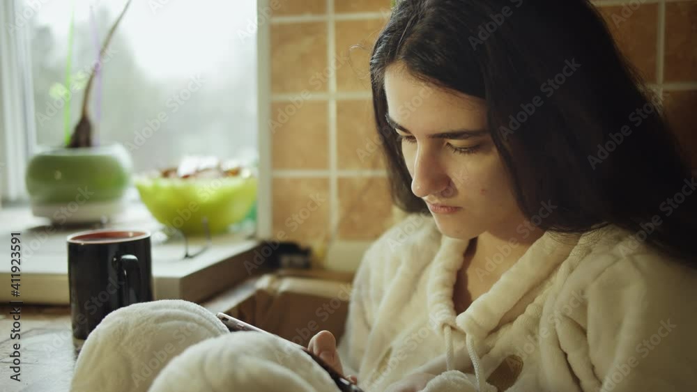 Girl brunette sits comfortably at the kitchen table with a mobile phone, camera tracking Girl brunette sits comfortably at the kitchen table with a mobile phone, camera tracking