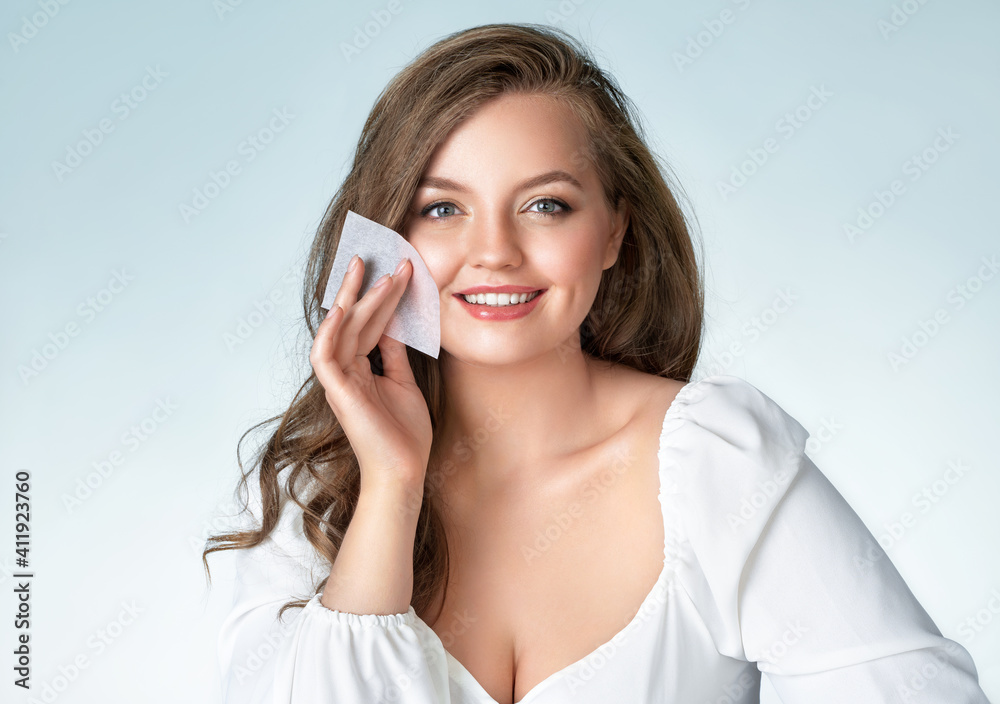 Fototapeta premium Woman using facial oil blotting paper. Photo of woman with perfect makeup on light blue background. Beauty and Skin care concept. Plus size model.