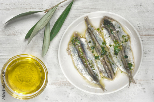 Pickled anchovies or sardines fillet in oil with herbs  and olive branch for tapas or antipasti on the white wooden background photo