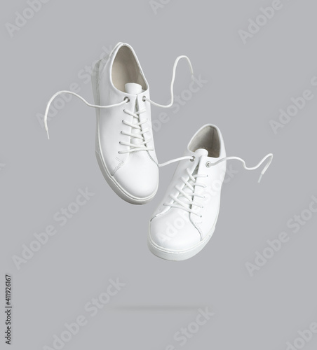 Flying white leather womens sneakers isolated on gray background. Fashionable stylish sports casual shoes. Creative minimalistic layout with footwear Mock up for your design Advertising for shoe store