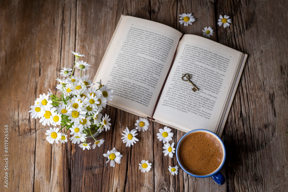 A cup of coffee with a book and daisies