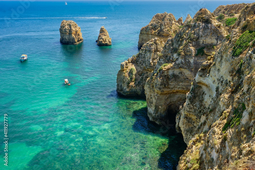 ACANTILADO EN EL ALGARVE DE PORTUGAL CON BARCO SOBRE EL AGUA CRISTALINA AZUL TURQUESA DEL OCEÁNO ATLÁNTICO