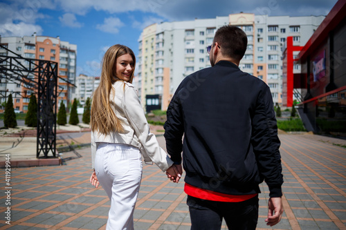Stylish young girl with blond hair of European appearance and a guy in a black jacket. Urban walk of a couple in love  modern fashion in casual style. Happy relationship concept