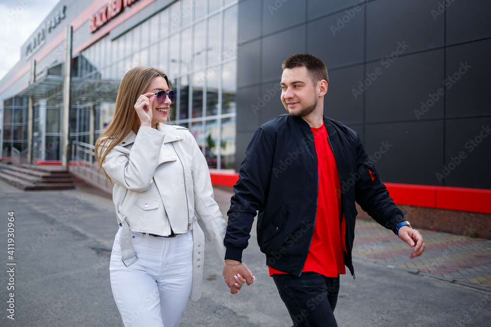Stylish young girl with blond hair of European appearance and a guy in a black jacket. Urban walk of a couple in love, modern fashion in casual style. Happy relationship concept Stylish young girl with blond hair of European appearance and a guy in a black jacket. Urban walk of a couple in love, modern fashion in casual style. Happy relationship concept