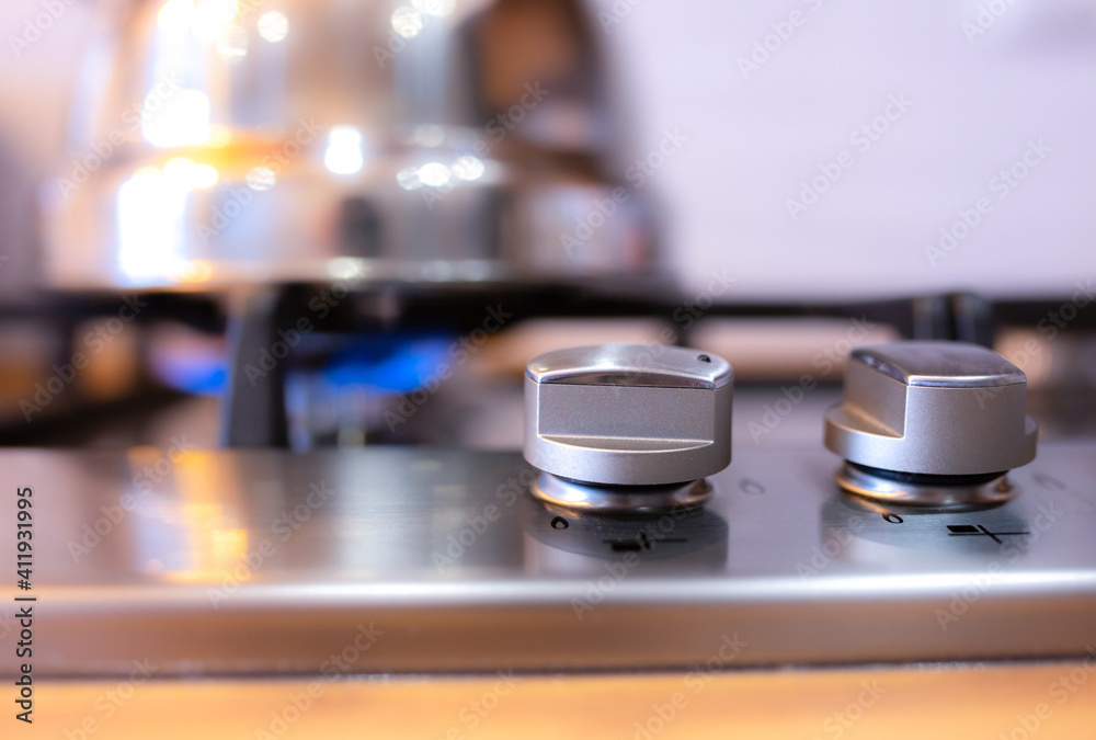 Turning on the gas stove in the kitchen. A metal silver teapot warming on a gas. Turning on the gas stove in the kitchen. A metal silver teapot warming on a gas.