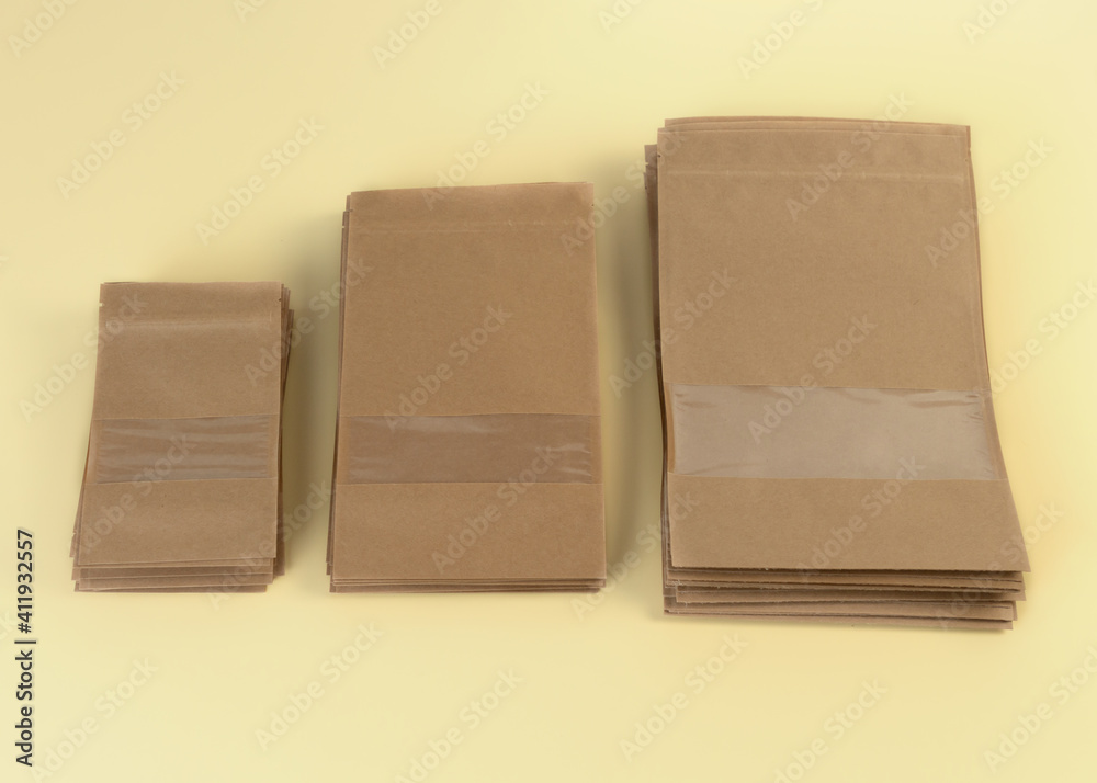 Brown kraft paper doypack bags with groceries front view on a yellow background. Packaging for foods and goods template mock-up. Packs with windows for weight products. Brown kraft paper doypack bags with groceries front view on a yellow background. Packaging for foods and goods template mock-up. Packs with windows for weight products.