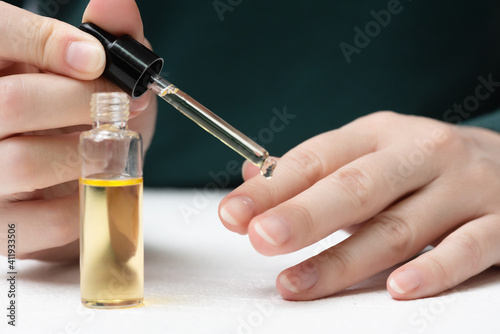 Woman is applying a cuticle oil on her fingernails close up.