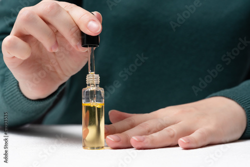 Woman is applying a cuticle oil on her fingernails close up.