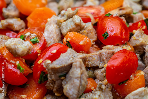 Fried juicy pieces of pork meat, tomatoes, garlic, green onions and spices. Shallow depth of field.Top view. Macro