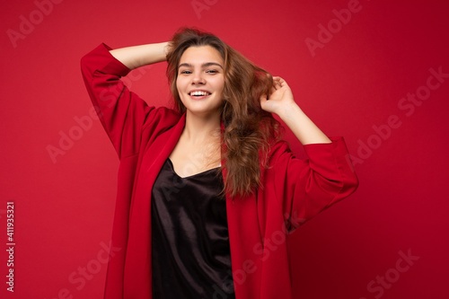 Young beautiful european stylish brunette woman wearing black blouse top and red cardigan isolated over red background with positive sincere emotions. Simple and natural looking at the camera. Free