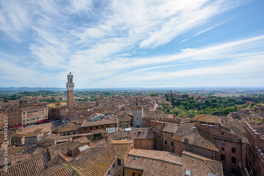 Panorama of Siena old town at sunrise, a medieval and Renaissance city in Tuscany, Italy, with Mangia tower and piazza del Campo, a church, old houses and palaces on a green hill