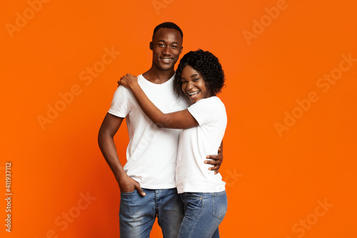 Joyful black couple in love hugging on orange