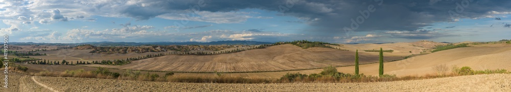 Panorama of Tuscan hills and badlands in Val d'Orcia, near Siena medieval town in Tuscany, Italy, with cypress trees, cultivated crop hills and farm houses in the countryside.