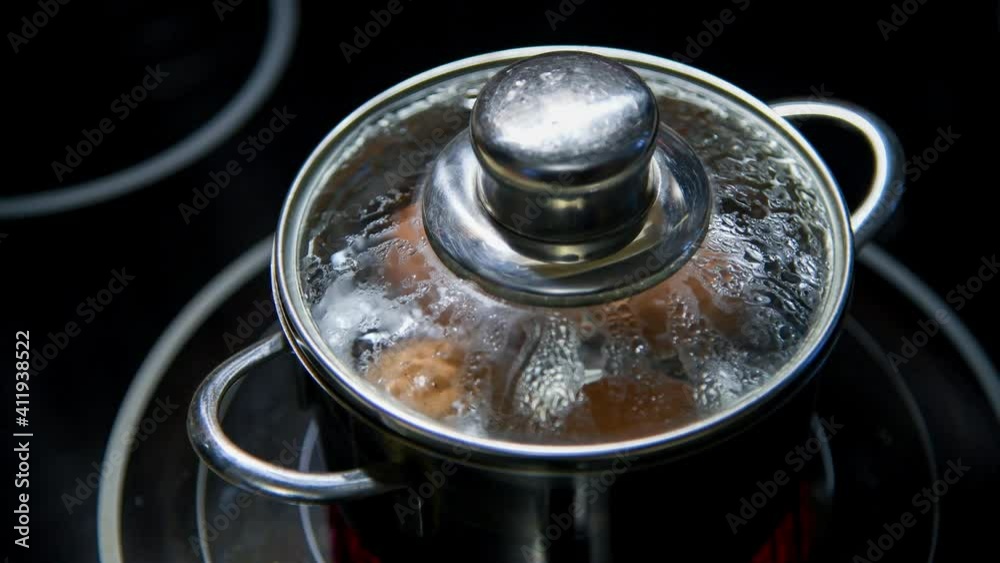 HD video. Close-up view of four brown chicken eggs boiling in hot water in small stainless saucepan on black kitchen stove (induction cooktop). Easter preparation theme. HD video. Close-up view of four brown chicken eggs boiling in hot water in small stainless saucepan on black kitchen stove (induction cooktop). Easter preparation theme.