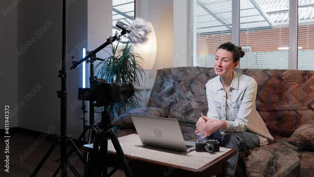Woman blogger or vlogger streaming online on social media to her subscribers. Woman using microphone, video camera and other blogging set ups at her house while talking on camera.