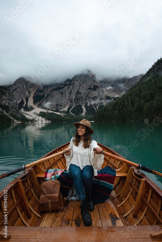 Happy tourist woman with hat sitting in a wooden boat on Braies lake surrounded by the mountains of the Italian Alps 