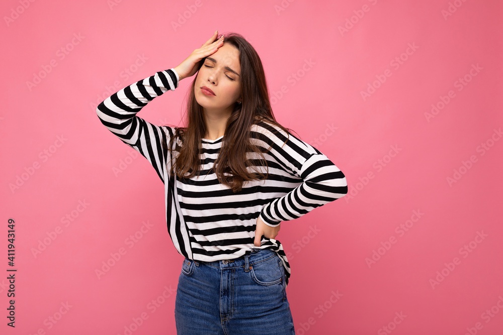 Photo of young sad upset tired beautiful brunette woman with sincere emotions wearing casual striped pullover isolated on pink background with copy space and having headache Photo of young sad upset tired beautiful brunette woman with sincere emotions wearing casual striped pullover isolated on pink background with copy space and having headache