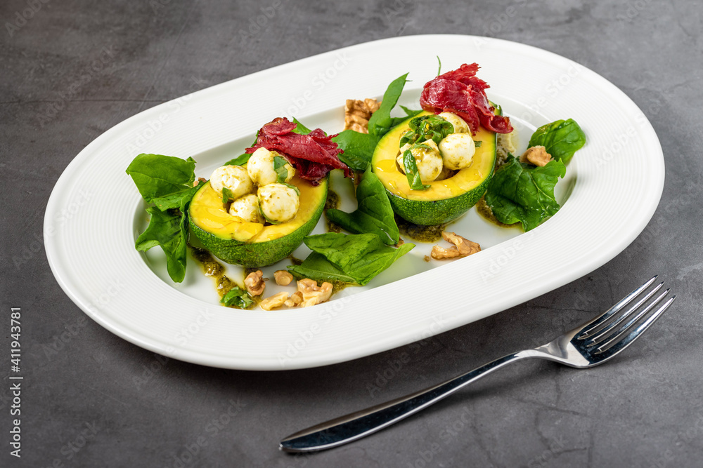 Bocconcini cheese balls in halves of avocado served with salad on white plate Bocconcini cheese balls in halves of avocado served with salad on white plate