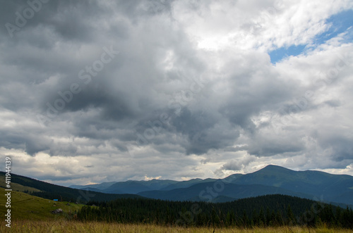 A scenic view of the mountains landscape, forest, meadows and pasture on the background with a cloudy sky covering the Carpathian ridge, Ukraine