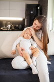 Young mother with sleeping baby on hands on couch at home