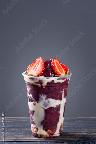 Brazilian frozen açaí in a plastic cup with condensed milk and strawberry. Fruit from the Amazon. Copy space