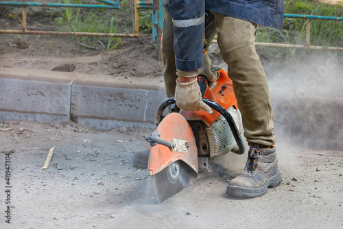 A worker uses a portable chainsaw and a diamond cutting disc to cut old asphalt on the road.