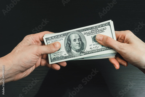 Male and female hand holding a wad of dollars on a black background close-up. Concept of bribery, assistance, and remuneration