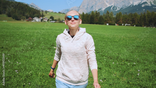 Blonde woman having fun by running in nature field in summer. Mountains in the background.