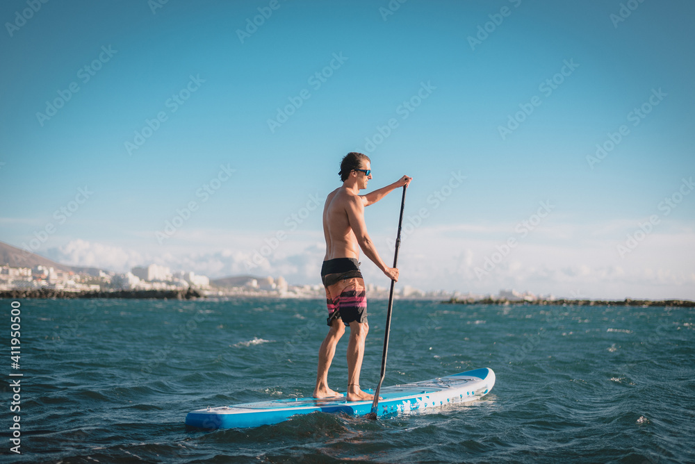 a young sportsman man practices paddle surfing on the beach under a blue sky a young sportsman man practices paddle surfing on the beach under a blue sky