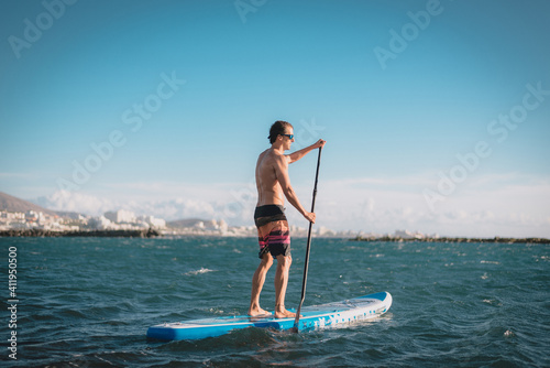 a young sportsman man practices paddle surfing on the beach under a blue sky