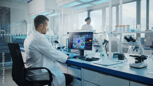 Advanced Medical Science Laboratory: Medical Scientist Working on Personal Computer with Screen Showing Virus Analysis Software User Interface. Scientists Developing Vaccine, Drugs and Antibiotics.