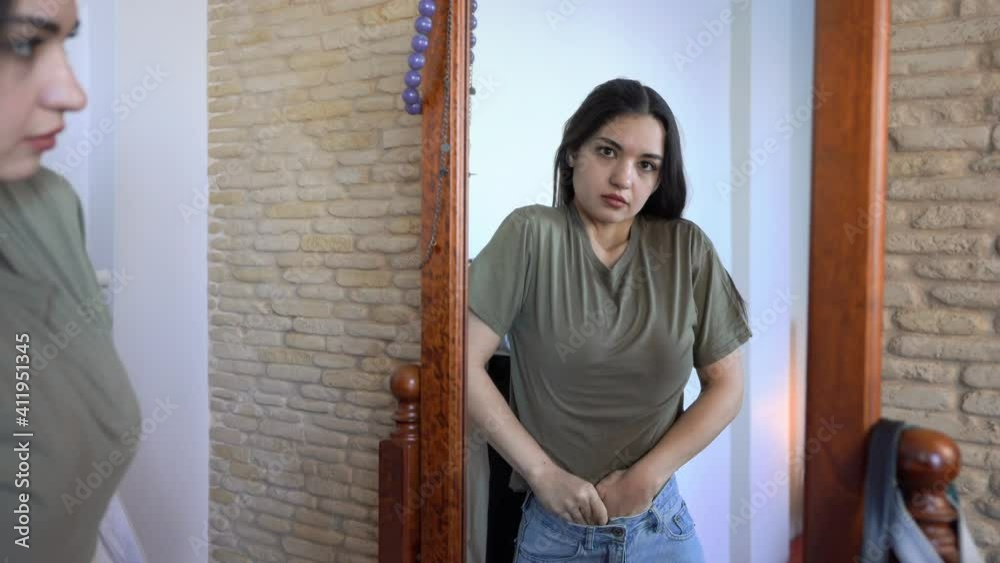 Attractive young woman is Looking in the mirror. Putting together outfit & tucking in a t-shirt Attractive young woman is Looking in the mirror. Putting together outfit & tucking in a t-shirt