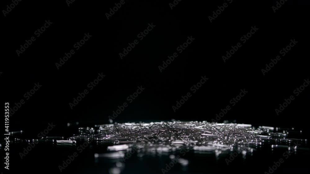 Stainless paper clips falling down on the mirror surface on black background Stainless paper clips falling down on the mirror surface on black background