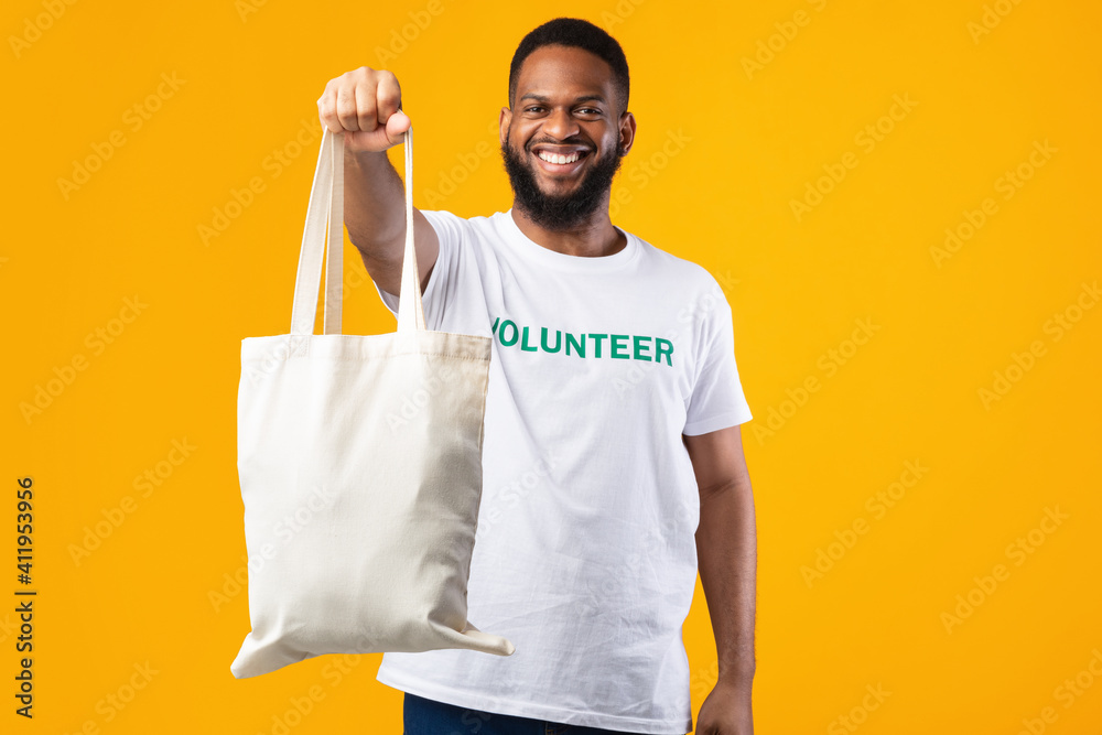 African Volunteer Man Showing Eco Bag To Camera, Yellow Background African Volunteer Man Showing Eco Bag To Camera, Yellow Background